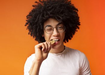 Cryptocurrency value. Millennial african-american guy biting golden bitcoin, orange studio background